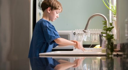 Ung gutt vasker hendene i kjøkkenvask