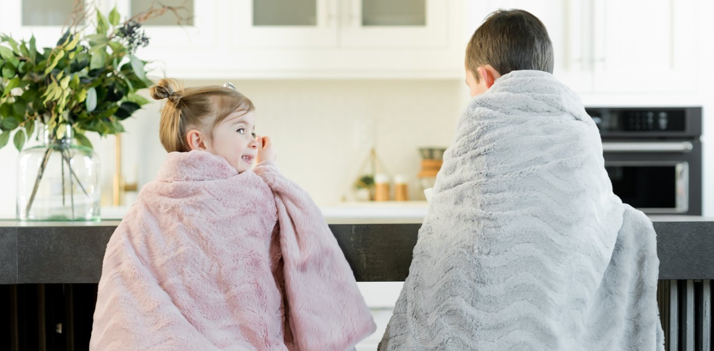 To barn under pledd på stoler ved kjøkkenbenken